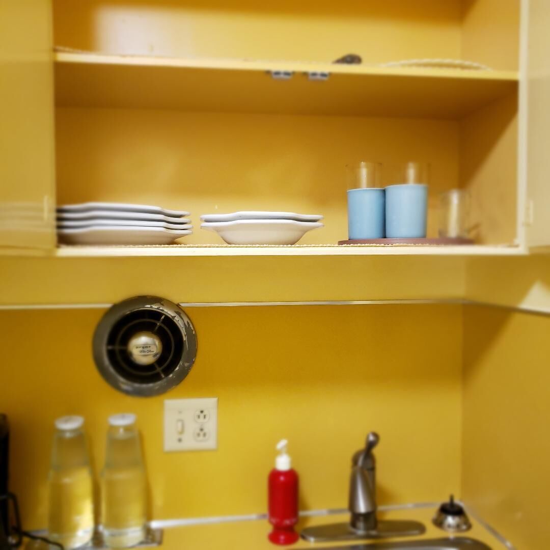 Un baño amarillo con lavamanos, grifo y dispensador de jabón. También hay dos botellas de líquido y un espejo.