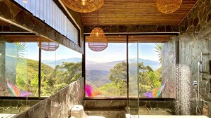 Une salle de bain avec un lavabo en pierre, des toilettes et une baignoire. De grandes fenêtres offrent une vue sur un paysage montagneux.