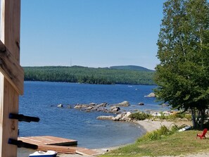 A lakeside view with a dock, a red chair, and a wooden structure. - A beautiful place to bring your family! (Dedham)