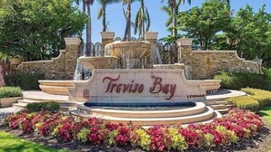 Una fuente con la inscripción "Travis Bay" rodeada de jardines cuidados y palmeras.