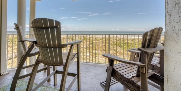 A wooden deck with two Adirondack chairs facing a beach.