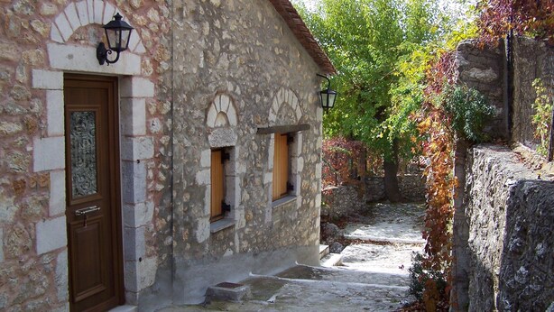 A stone building with a wooden door and two windows, a stone wall with ivy, and a cobblestone path.