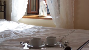 A neatly made bed with a cup and saucer set on a tray, a spoon, and a small white lantern on the windowsill.
