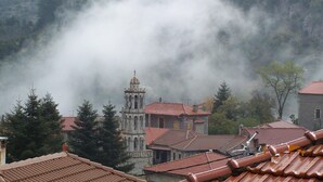A mountainous village with a prominent church featuring a bell tower, surrounded by residential buildings with red-tiled roofs.