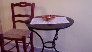 A small round table with a white cloth and two bowls on it, a wooden chair with a cushion, and a plain wall in the background.