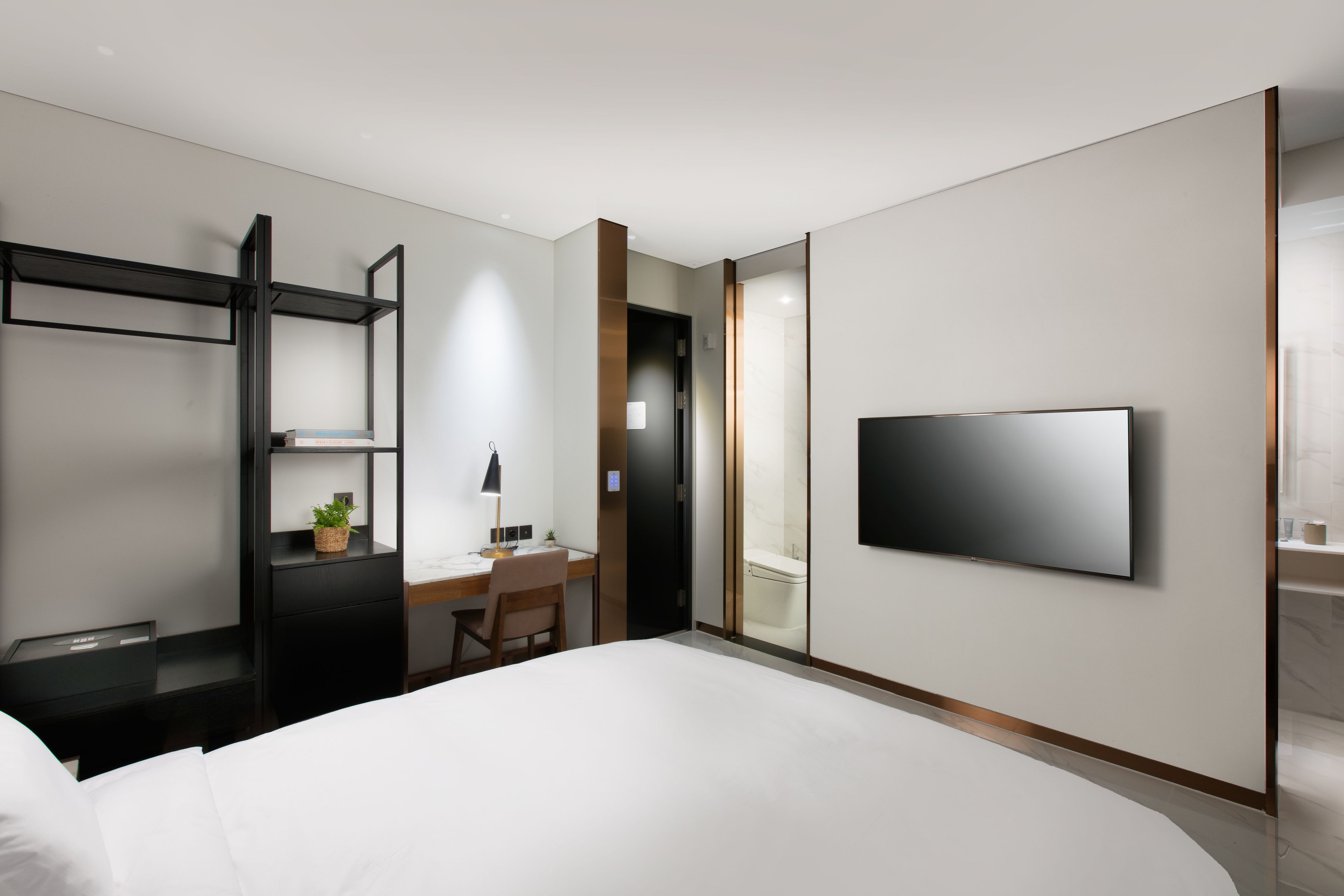 Een moderne hotelkamer met een bed, bureau, stoel, televisie en een kleine plant.