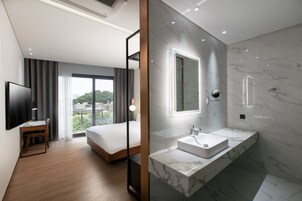 Una habitación de hotel moderna con una cama grande, un escritorio, un televisor y un baño con lavabo y ducha de mármol.