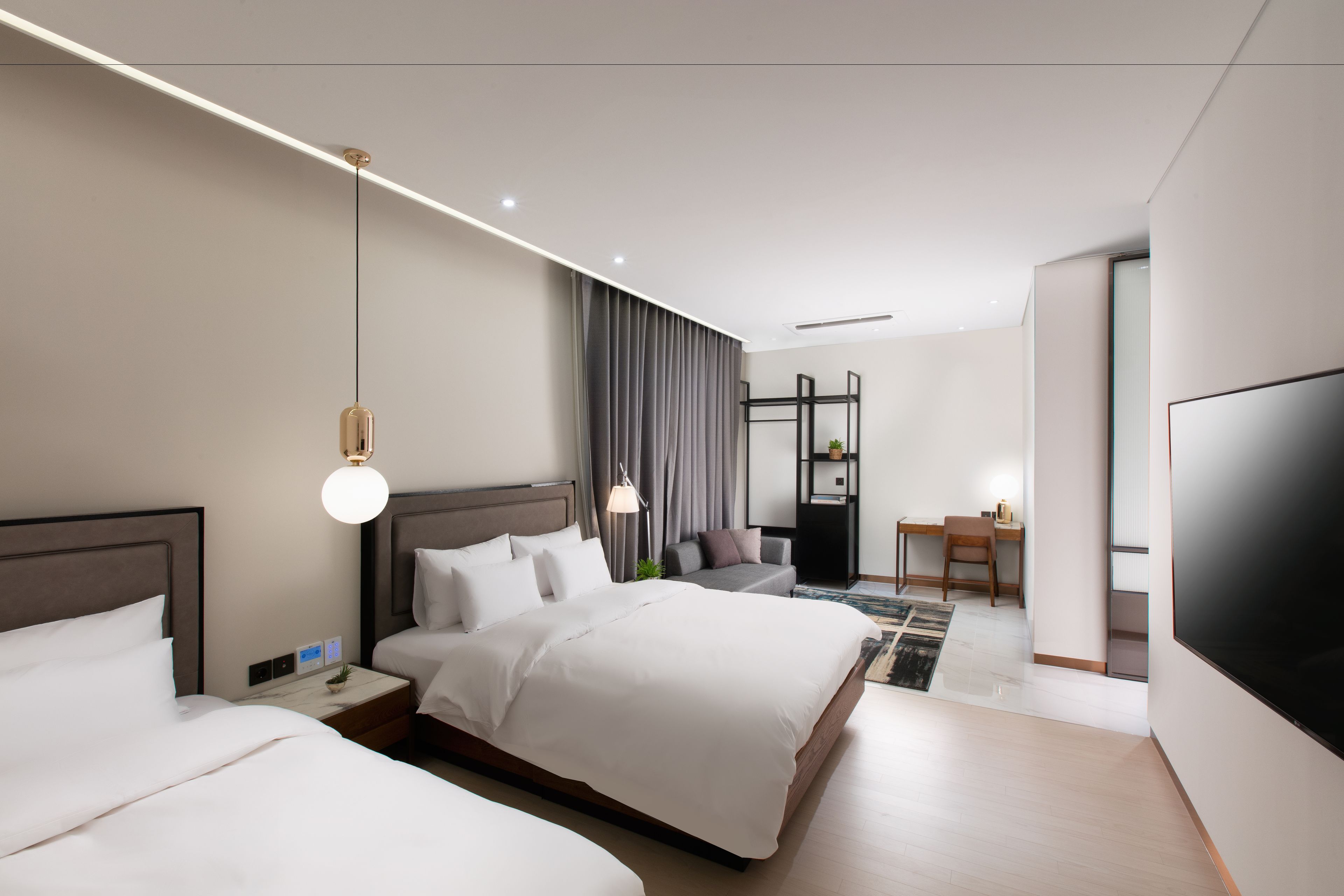 A modern hotel room with two beds, a desk, and a TV.