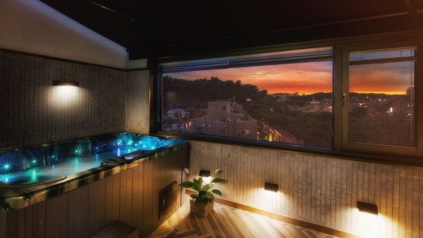 Une salle de bain moderne dotée d’une grande fenêtre, d’un meuble-lavabo en bois et d’une baignoire de type spa avec éclairage bleu.