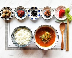 Variedad de platos, incluyendo un tazón de arroz, un tazón de sopa y varias pequeñas bandejas con diferentes alimentos.