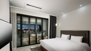 Une chambre d’hôtel moderne dotée d’un grand lit, d’une télévision à écran plat, d’un balcon offrant une vue sur la ville et d’une porte-fenêtre coulissante.