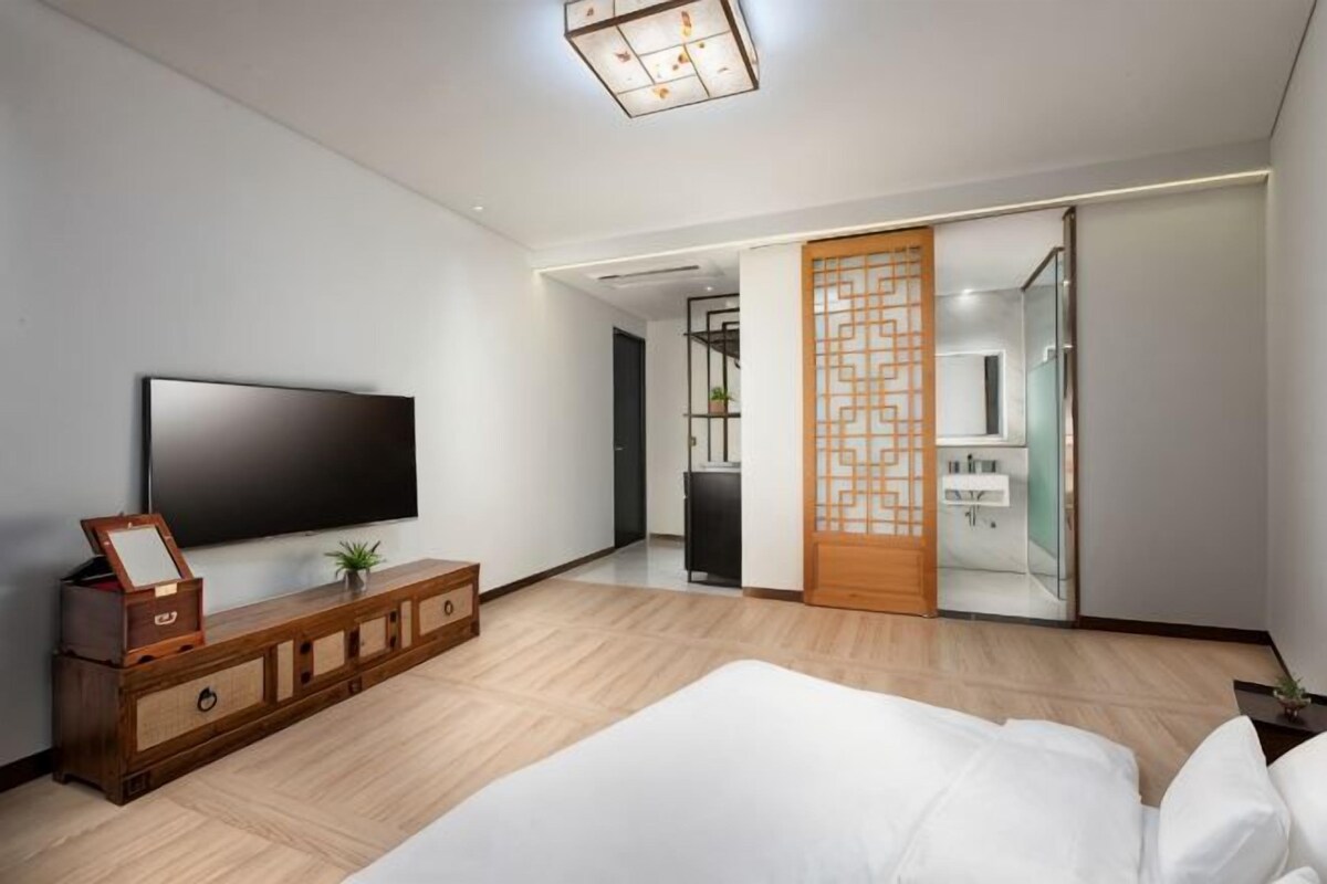 Una habitación de hotel moderna con televisión de pantalla plana, muebles de madera, una cama y una puerta corredera que da al baño.