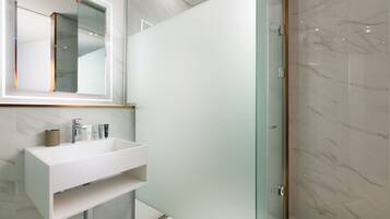 Un baño moderno con un tocador blanco, cabina de ducha de vidrio y pared revestida de mármol.
