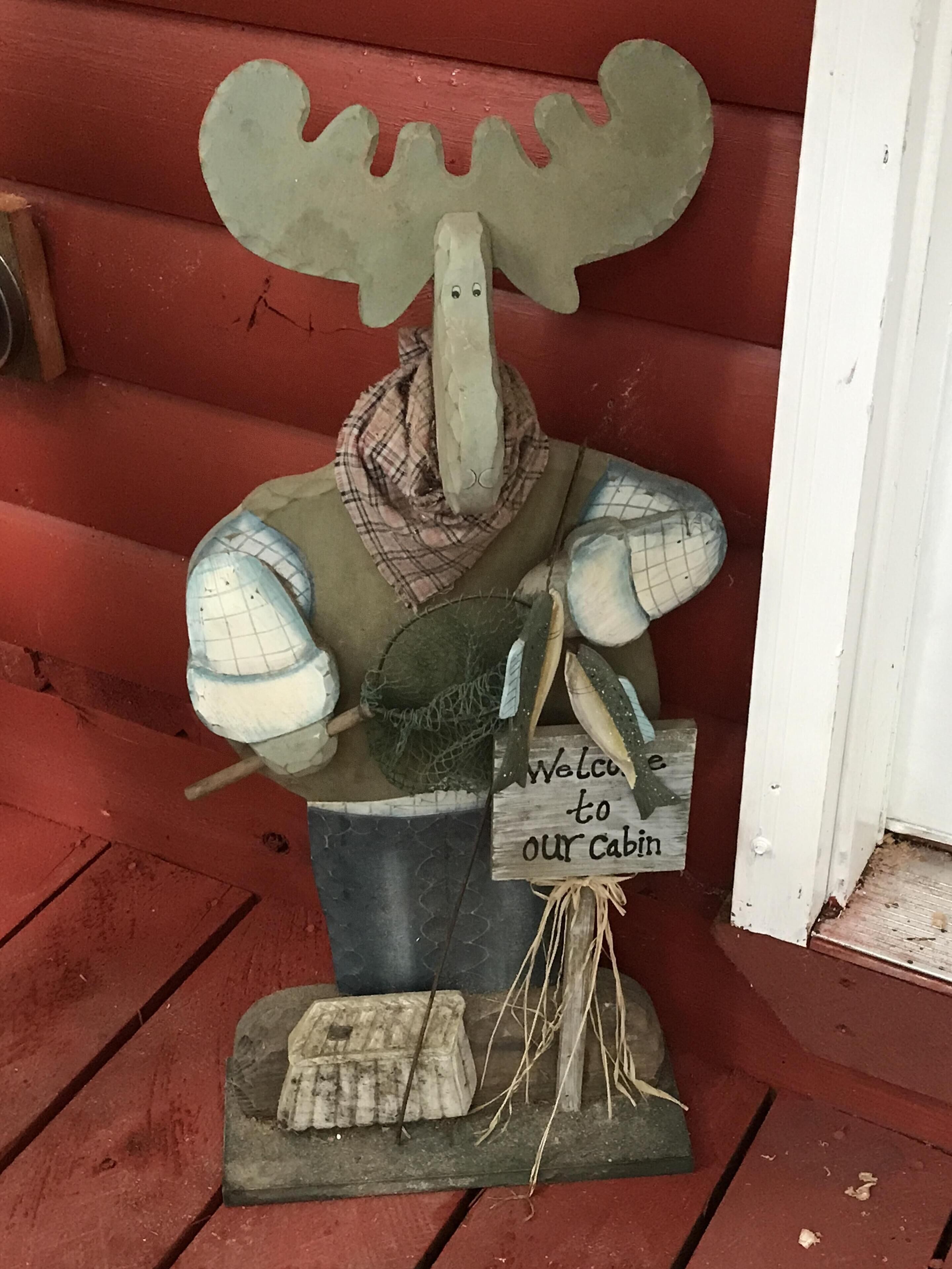 A rustic cabin with a moose decoration, a plaid scarf, and a welcome sign.