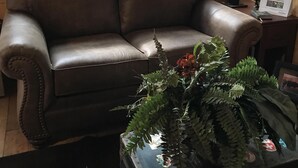 A brown leather sofa, a potted plant, and a lamp in a room with wooden walls and a window. - Experience Alaska with a touch of home! (Hollis)