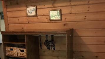 A wooden wall with two framed pictures, a wooden shelf with baskets, and a hanging rack with utensils.
