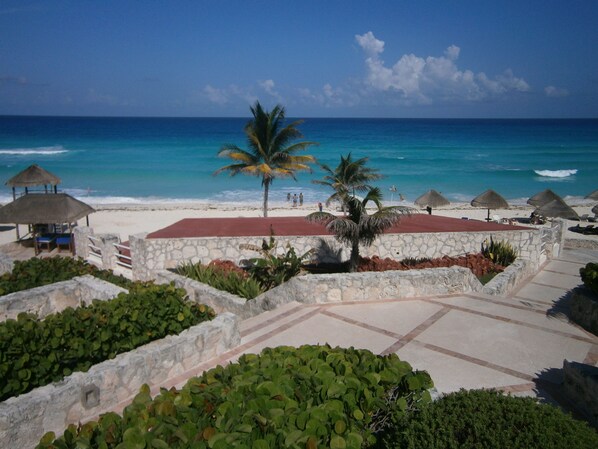 A beach resort with a stone wall, palm trees, and thatched umbrellas. - Beach Resort in Zona Hotelera Cancun Amenities Included
Beach, Pool, Kitchen, (Zona Hotelera)
