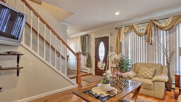A spacious living room with a wooden staircase, a television mounted on the wall, a sofa, and a coffee table with decorative items. - Charming One Family Colonial Home / Business . (East Orange)