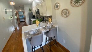 A modern kitchen with white cabinets, a central island with bar stools, and decorative wall art. - Charming One Family Colonial Home / Business . (East Orange)