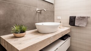 Une salle de bain moderne avec un meuble-lavabo en bois, un lavabo sur colonne blanc, une petite plante en pot et un porte-serviettes.