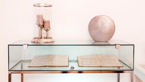 Une vitrine en verre contenant deux livres ouverts et un objet cylindrique.