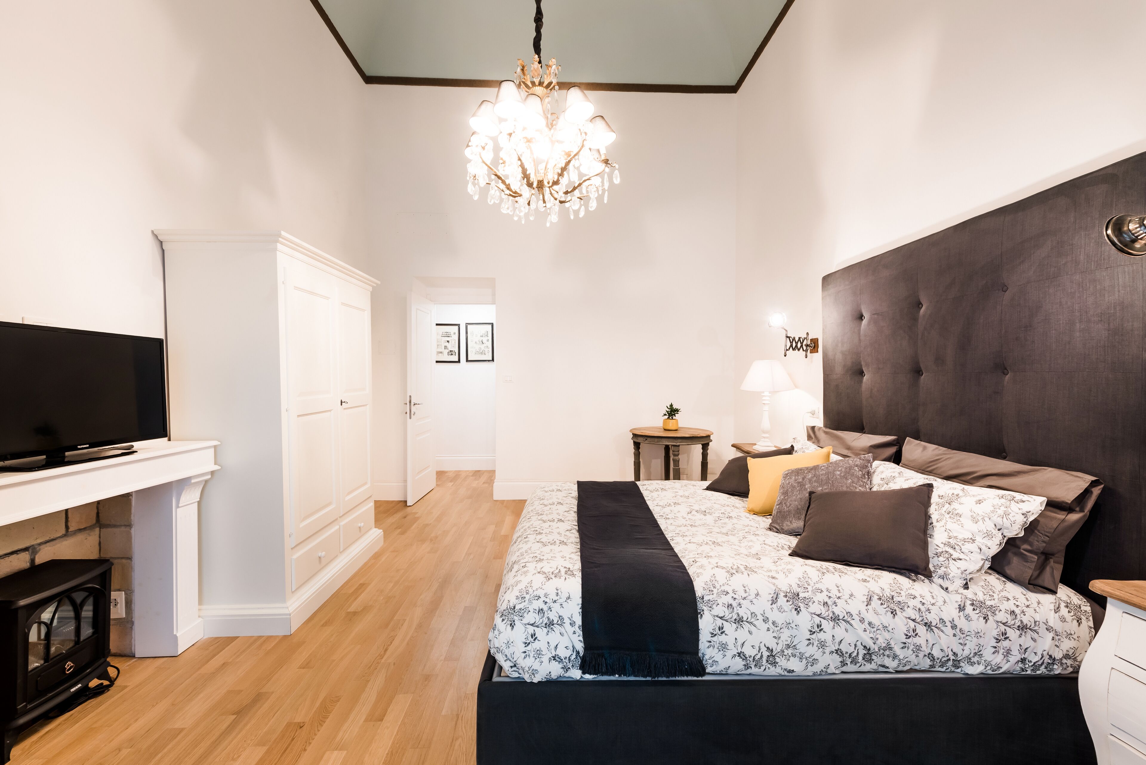 A bedroom with a bed, a television, a chandelier, and a white wardrobe.