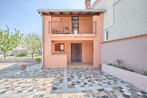 Stylish two-story residence with a balcony and a ground-floor patio area featuring potted plants.