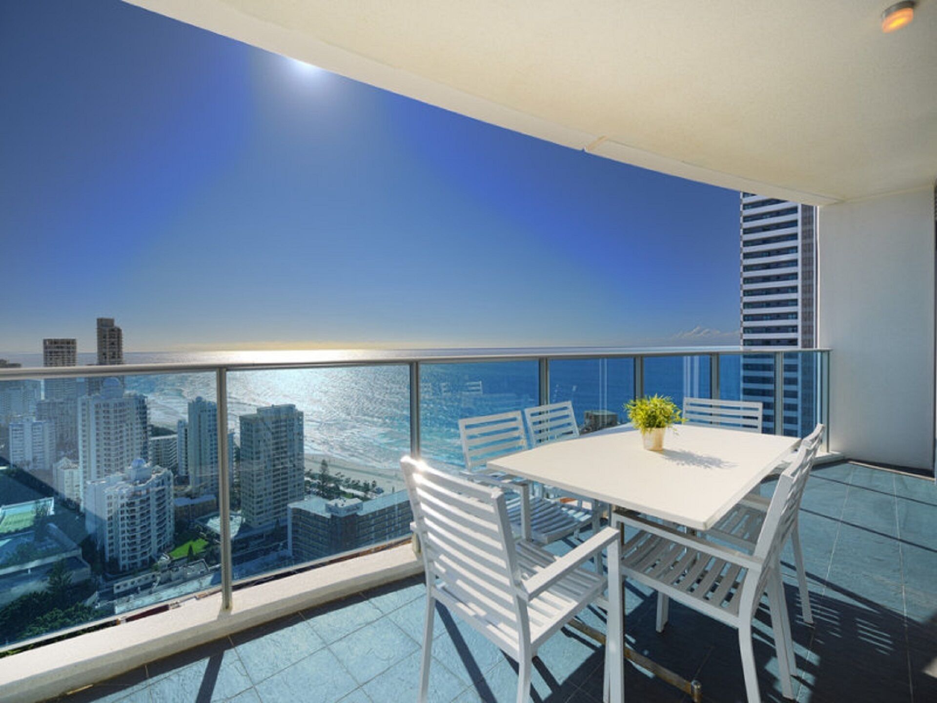A balcony with a white table and chairs, a potted plant, and a city view.
