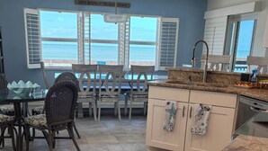 Une cuisine avec vue sur l’océan, un coin repas avec des chaises en osier et un sol carrelé.