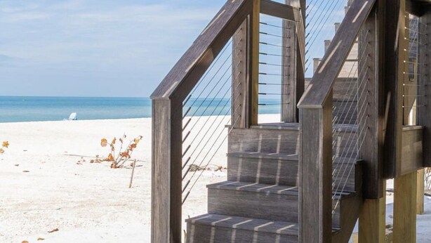 Un escalier en bois mène à une zone de plage d’où l’on a une vue dégagée sur l’océan.