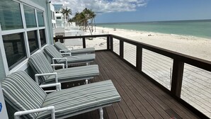 Une terrasse en bois avec des chaises longues à rayures et vue sur la plage.
