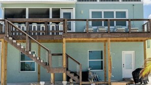 Une maison de plage à deux étages, dotée d’un balcon, d’un escalier en bois et d’une porte.