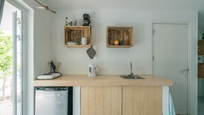 A compact kitchen with wooden cabinets, a built-in dishwasher, and two wooden shelves above the countertop. - 'Boutique' studio 'Dushi Bida' (Willemstad)