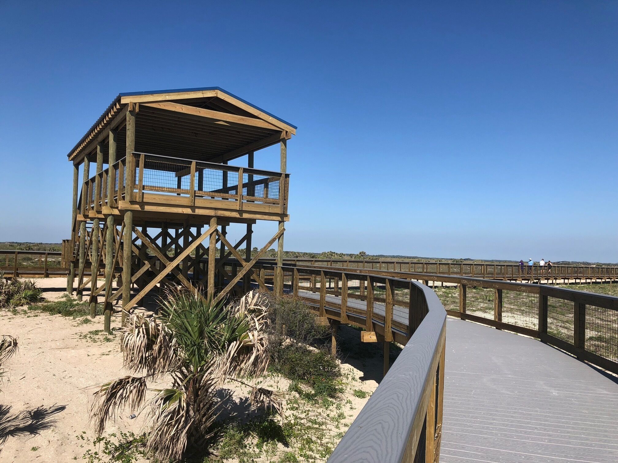 A wooden observation tower with a balcony, surrounded by a sandy beach and sparse vegetation.