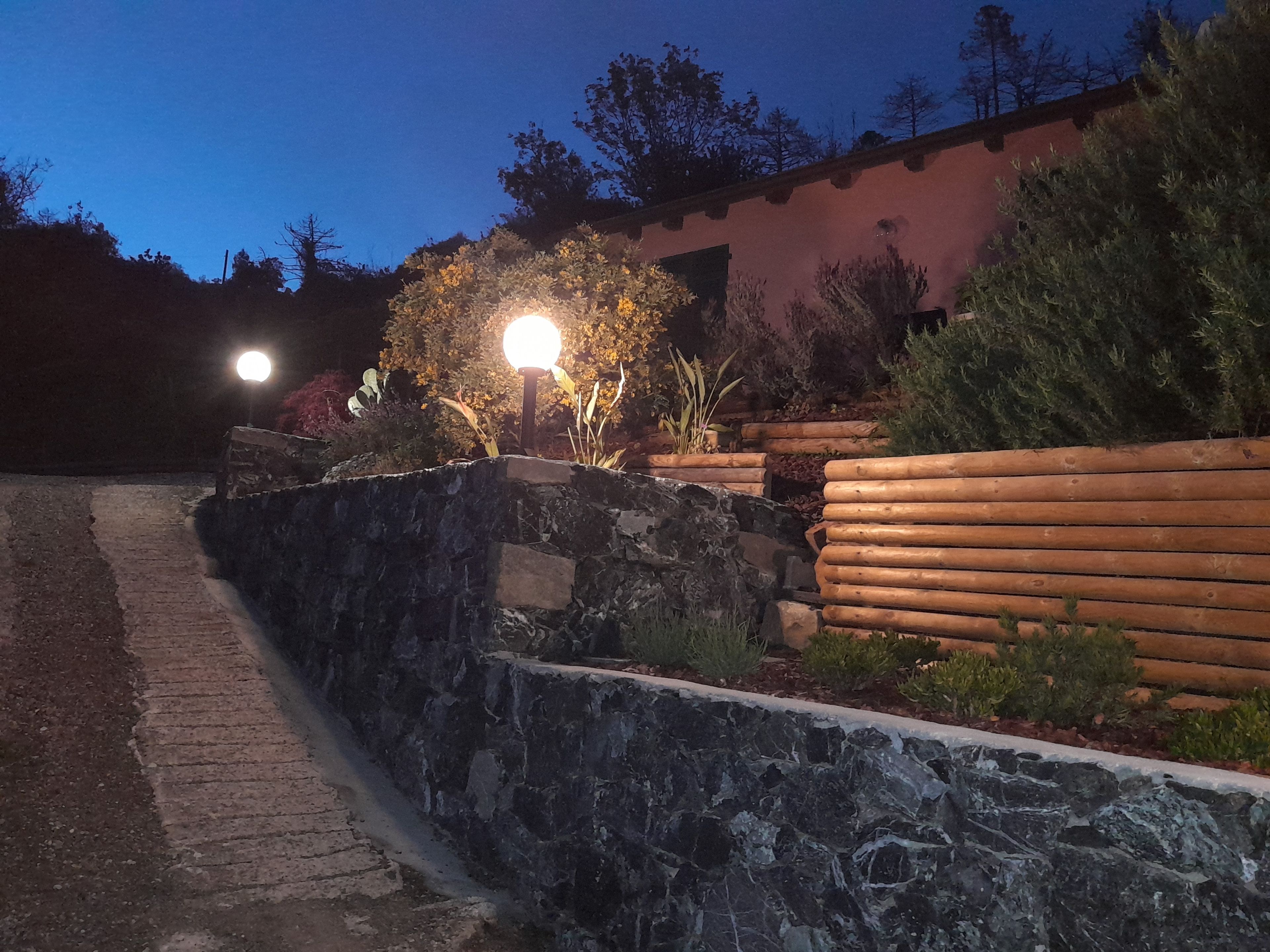 Un vialetto in pietra conduce a un edificio con un recinto in legno e un'area giardino ben illuminata.