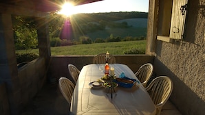 Tavolo apparecchiato per due con candela, una bottiglia e un cestino di pane su una terrazza con vista su un paesaggio suggestivo.
