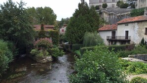 Un paesaggio tranquillo lungo il fiume, con edifici in pietra, vegetazione lussureggiante e un corso d'acqua sereno.