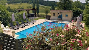 Una piscina con lettini e ombrelloni, immersa nel verde e con vista su dolci colline.