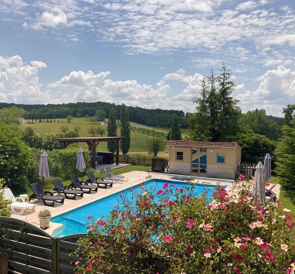 A swimming pool with lounge chairs and umbrellas, surrounded by greenery and a view of rolling hills.