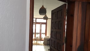 Una puerta de madera con un diseño geométrico, que da a una habitación con piso de baldosas y una lámpara colgante.