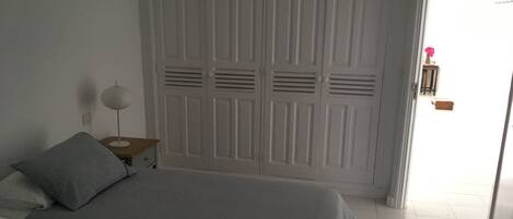 A bedroom with a bed, a nightstand, a lamp, and a wardrobe.