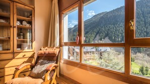 Una habitación con una mecedora de madera, un aparador con vajilla y un amplio ventanal con vistas a la montaña.