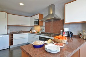 A modern kitchen with white cabinets, a stainless steel range hood, granite countertops, and a central island with food items.