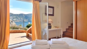A hotel room with a bed, a desk, a lamp, and a view of a mountainous landscape. - Charming Villa with Sea Views & Pool (Andratx)