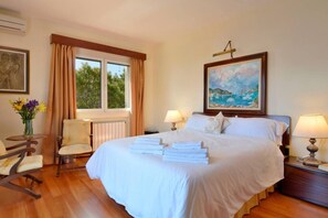 Een hotelkamer met een groot bed, twee nachtkastjes met lampen, een stoel, een raam met gordijnen en een schilderij aan de muur.