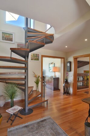A spacious living area with a modern spiral staircase, wooden flooring, and a view of the sky.