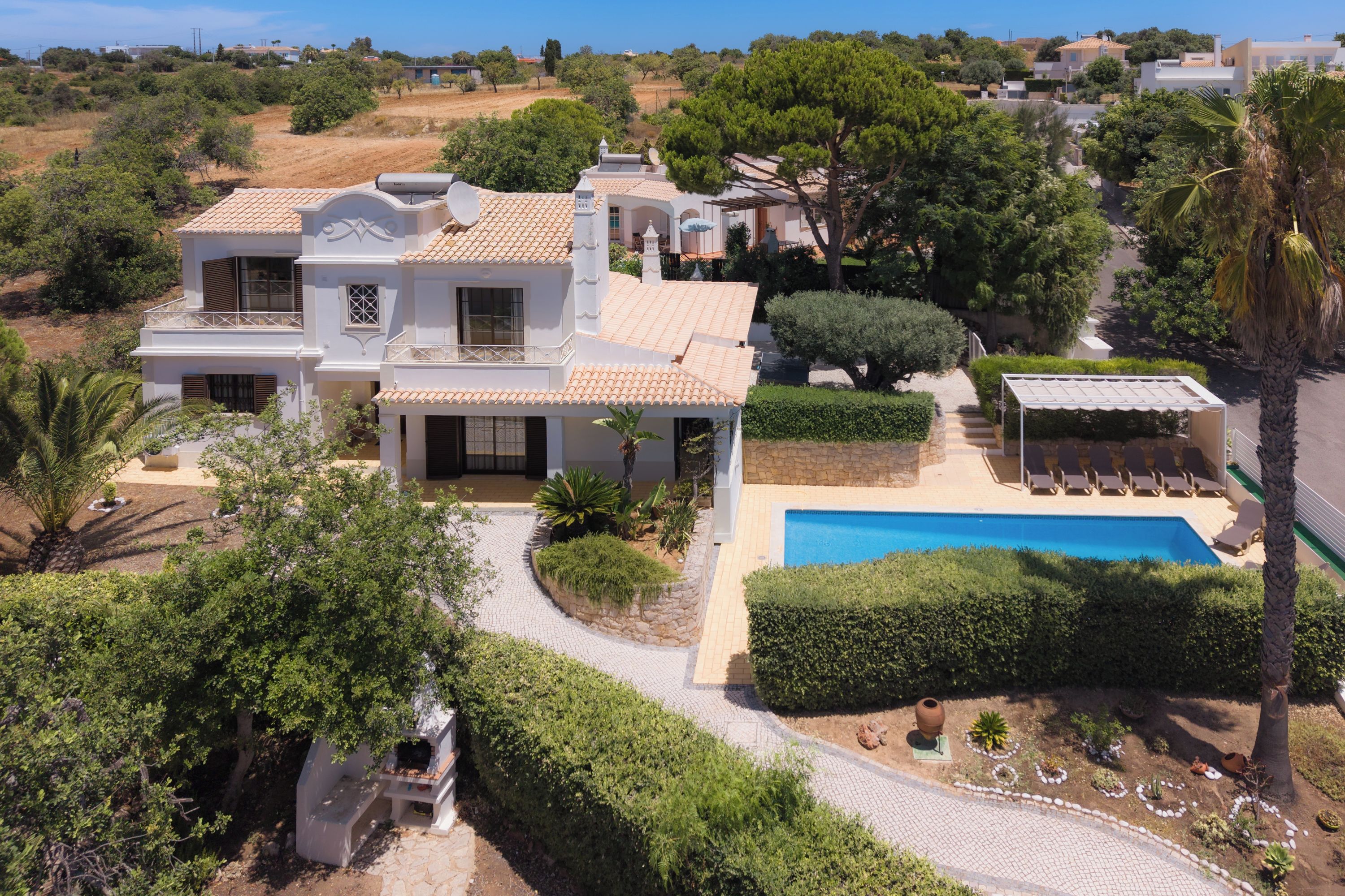 A large villa with a swimming pool, surrounded by lush greenery and a clear sky.