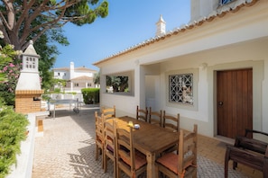 A patio with a wooden table and chairs, a brick structure, and a white building with a tiled roof. - Villa Ladeira - Private pool, Sea view, Smart tv, games, wifi, Ac (Albufeira)