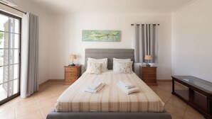 A neatly arranged bedroom with a bed, two bedside tables, a nightstand, a desk, and a window with curtains. - Villa Ladeira - Private pool, Sea view, Smart tv, games, wifi, Ac (Albufeira)