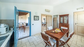 A dining area with a wooden table set for four, a kitchen with a blue-framed door, and a cabinet with glass doors.